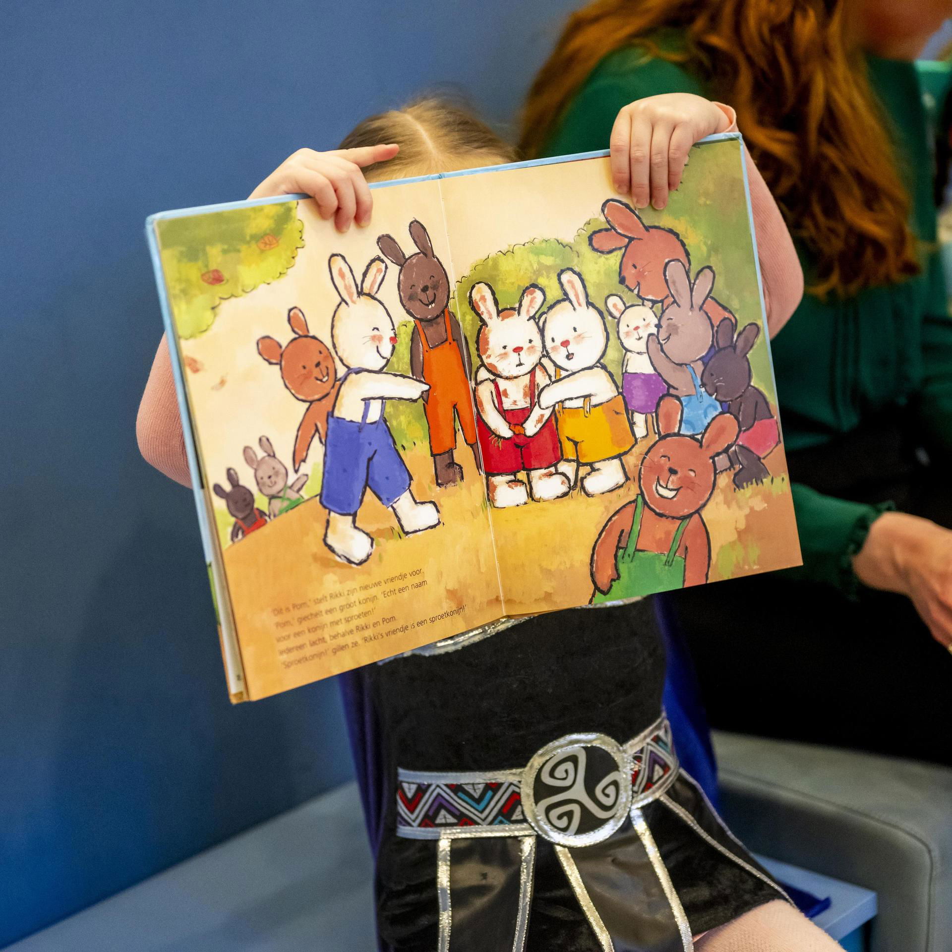 Meisje houdt een kleurrijk prentenboek voor haar gezicht.