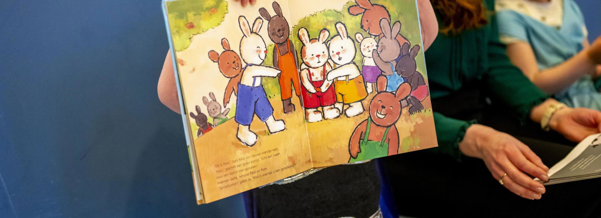 Meisje houdt een kleurrijk prentenboek voor haar gezicht.