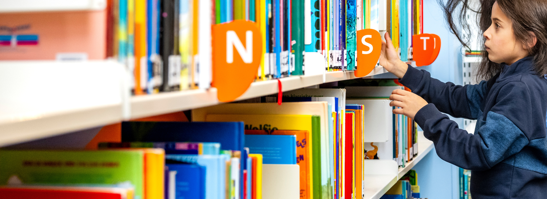 Jongen zoekt een boek uit de kast.